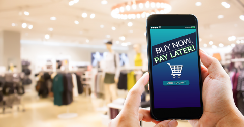BNPL Buy Now Pay Later online shopping; hand met mobiele telefoon en op de achtergrond een winkel